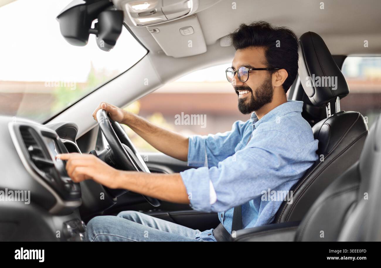 Un giovane indiano felice che guida un'auto e ascolta musica Foto Stock