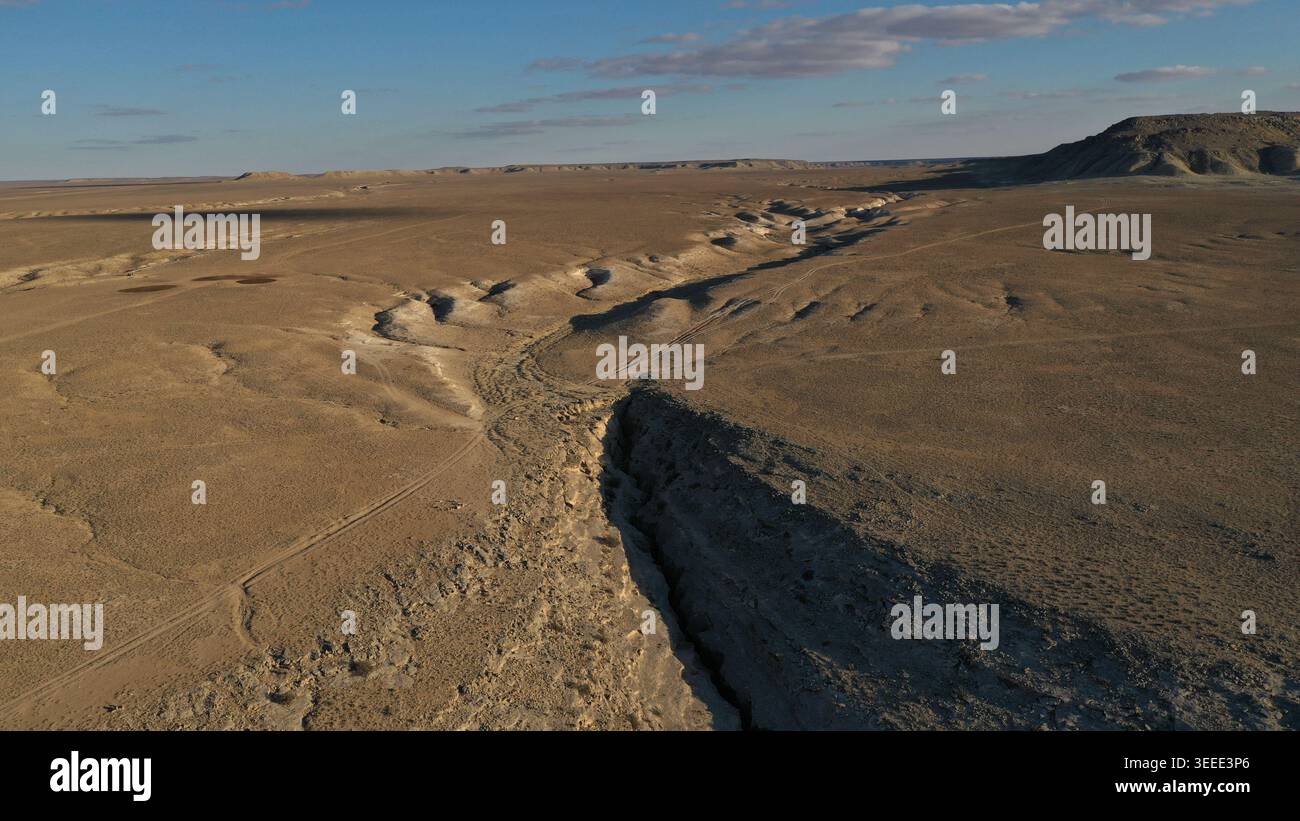 Una prospettiva aerea rivela un profondo canyon drammatico che si estende su un vasto e arido paesaggio desertico sotto un cielo azzurro limpido con nuvole sparse Foto Stock