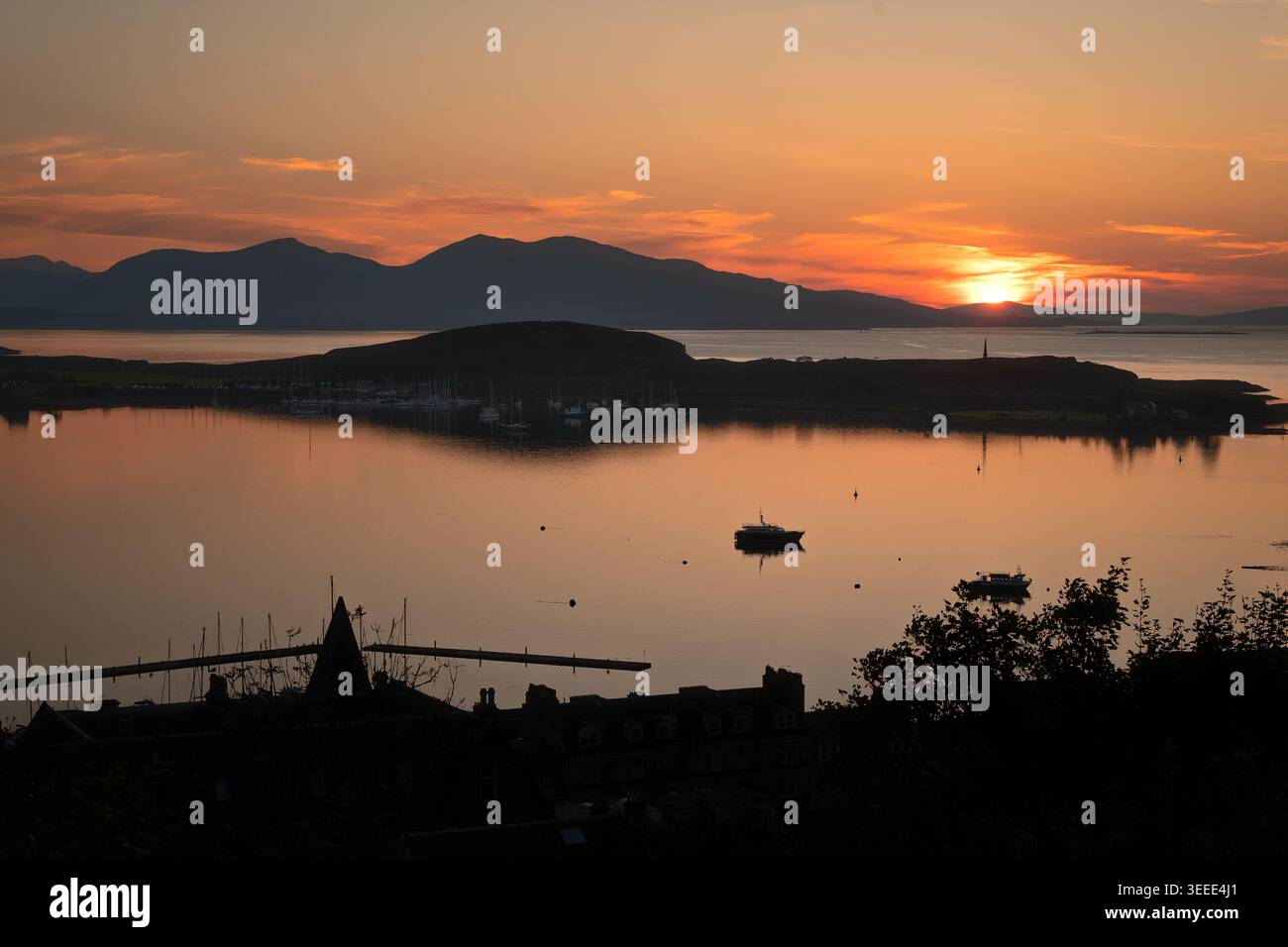 Vista calda del tramonto su acque calme, isole e lontane sagome di montagna a Oban, Scozia. Foto Stock