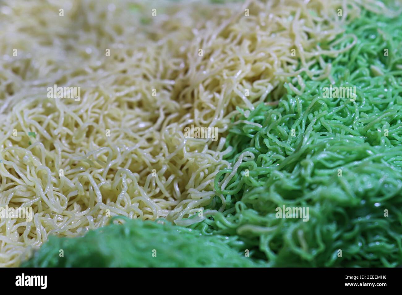 Primo piano di noodle all'uovo gialli crudi e filetti di giada verde. Consistenza lucida di pasta tradizionale asiatica e ingredienti di Street food. Foto Stock