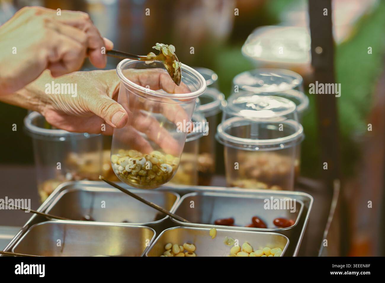 Mani che preparano chicchi misti per un sano frullato di cinque chicchi in un mercato tailandese che mostra nutrizione basata sulle piante e stile di vita benessere. Foto Stock