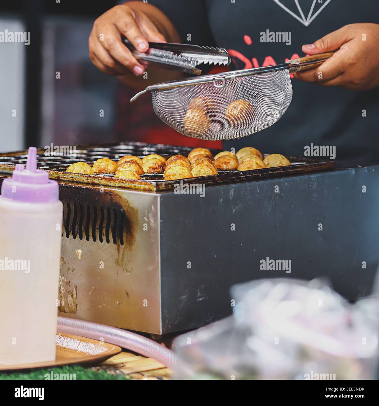 Cucina takoyaki in stile thailandese in un vivace mercato notturno con autentica atmosfera di Street food e preparazione all'azione Foto Stock