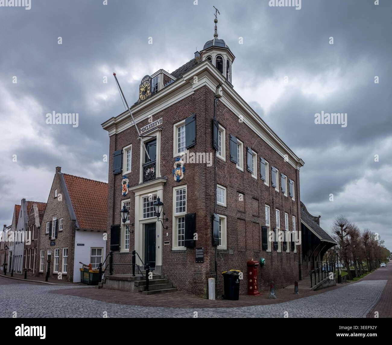 Sotto un cielo drammatico di nuvole di tempesta massiva, lo Stadhuis di Nieuwpoort presenta un contrappunto suggestivo alla sua veste più soleggiata. L'edificio e' di colore rosso Foto Stock