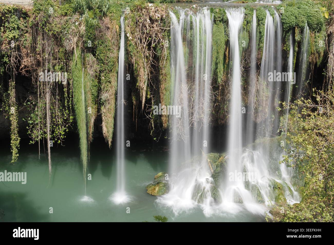 L'acqua scorre giù da alte rocce in una piscina verde sottostante Foto Stock