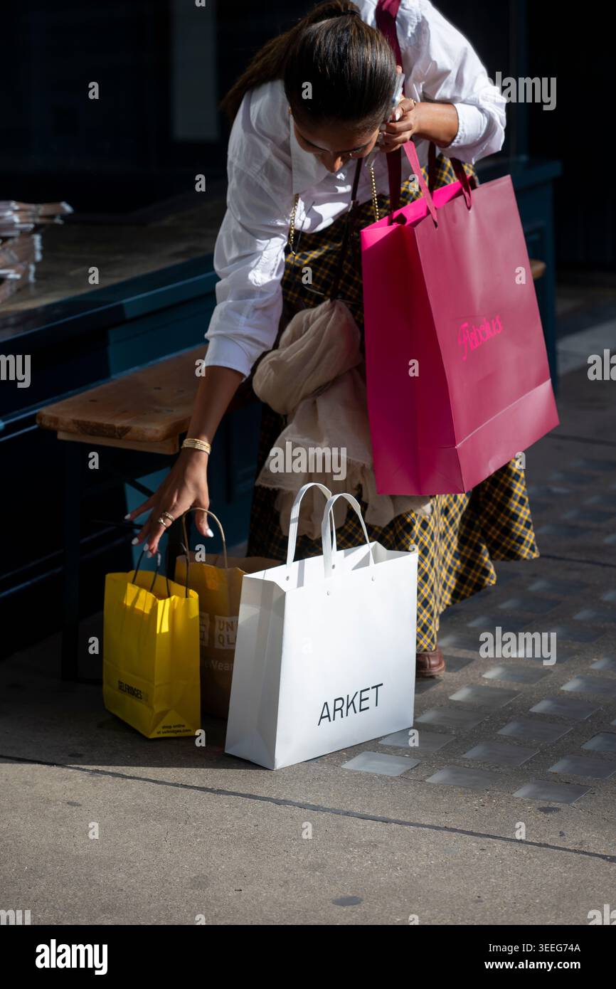 Acquirenti che collocano borse per la spesa di marca, tra cui Arket, nel quartiere dello shopping del West End di Londra. Foto Stock
