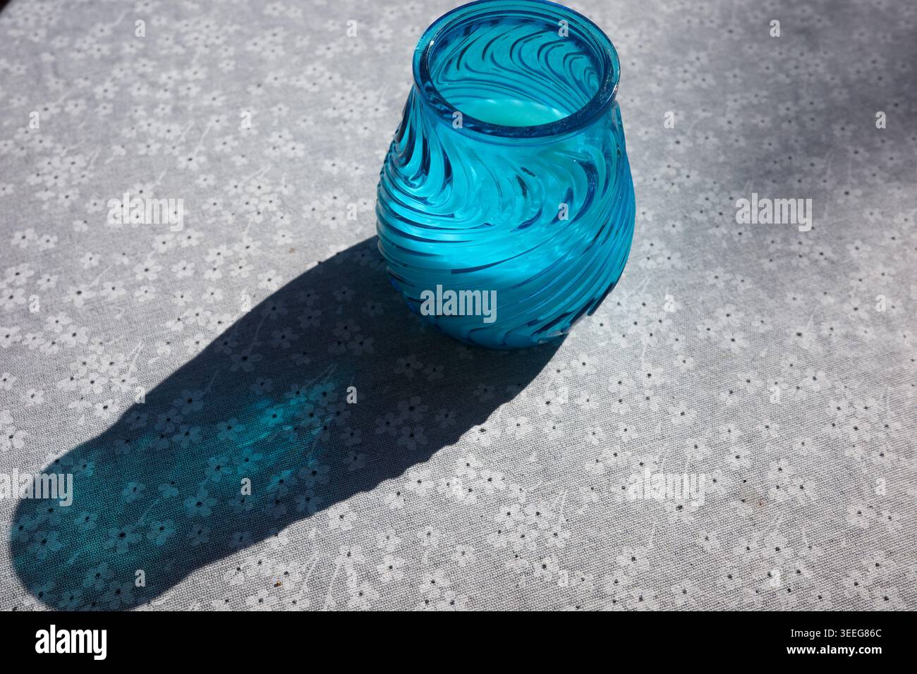 Vaso in vetro blu su tovaglia fantasia con ombra alla luce del sole Foto Stock