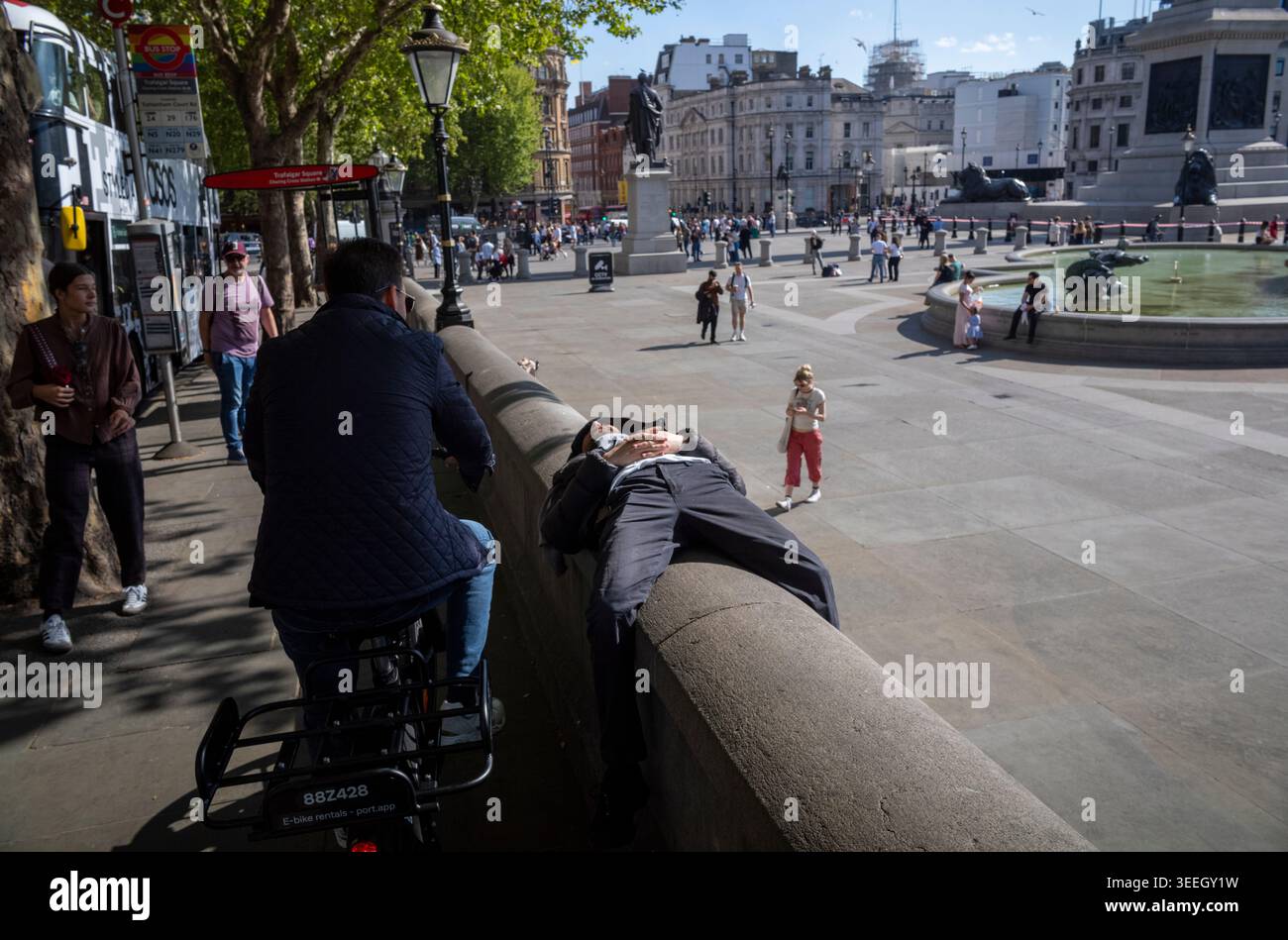 Un uomo adagiato su un muro che gode delle temperature estive a Trafalgar Square nel centro di Londra, maggio 2026, Inghilterra, Regno Unito Foto Stock
