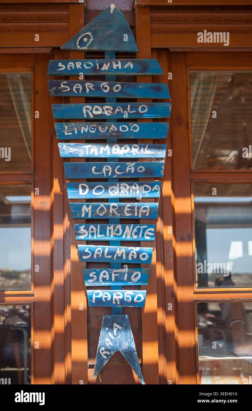 Menu di pesce offerto da un ristorante portoghese sulla spiaggia. Piatti dipinti su una struttura in legno a forma di pesce. Foto Stock
