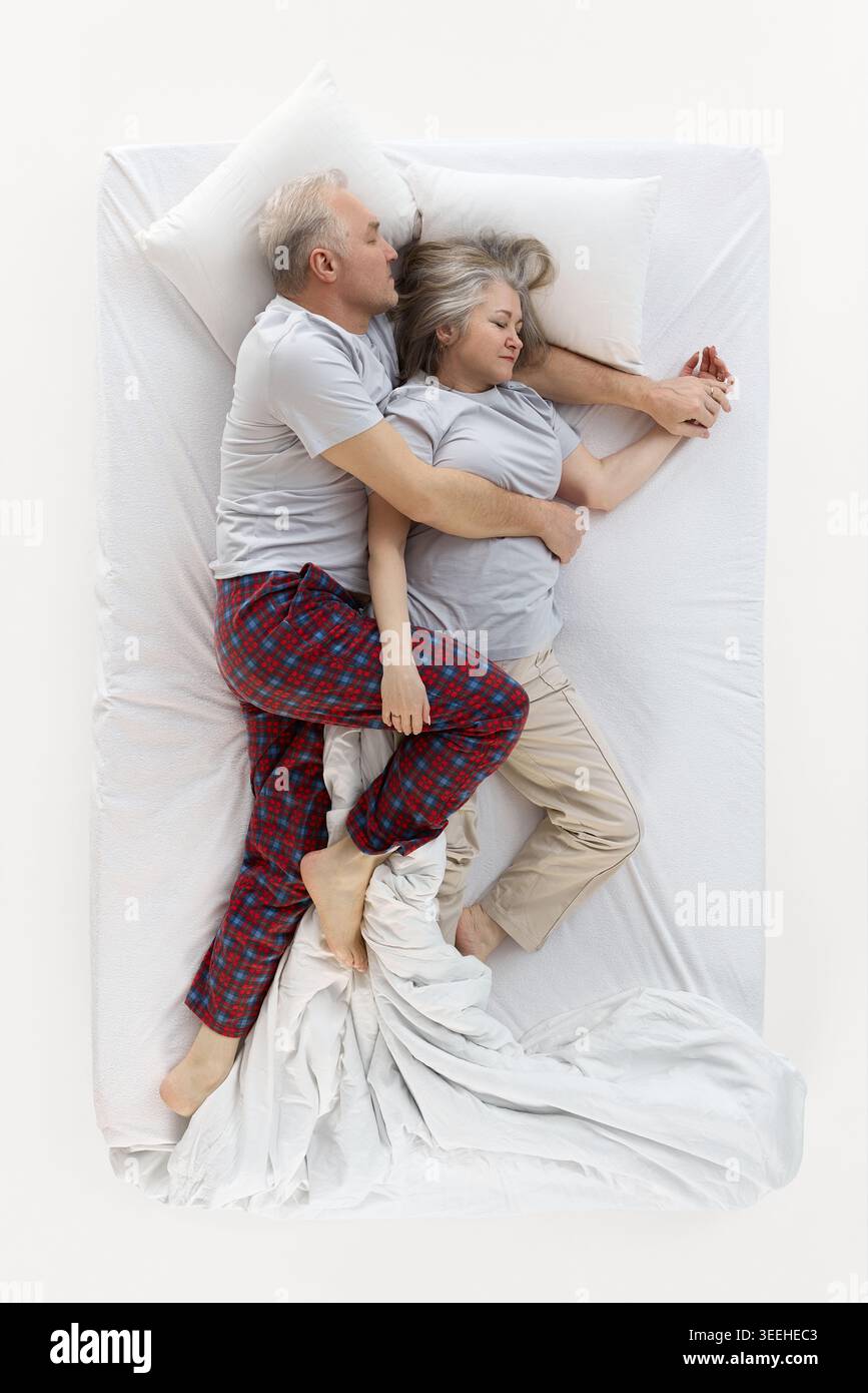 Uomo anziano che abbraccia la donna addormentata in posizione di spogliamento sul letto. Foto Stock