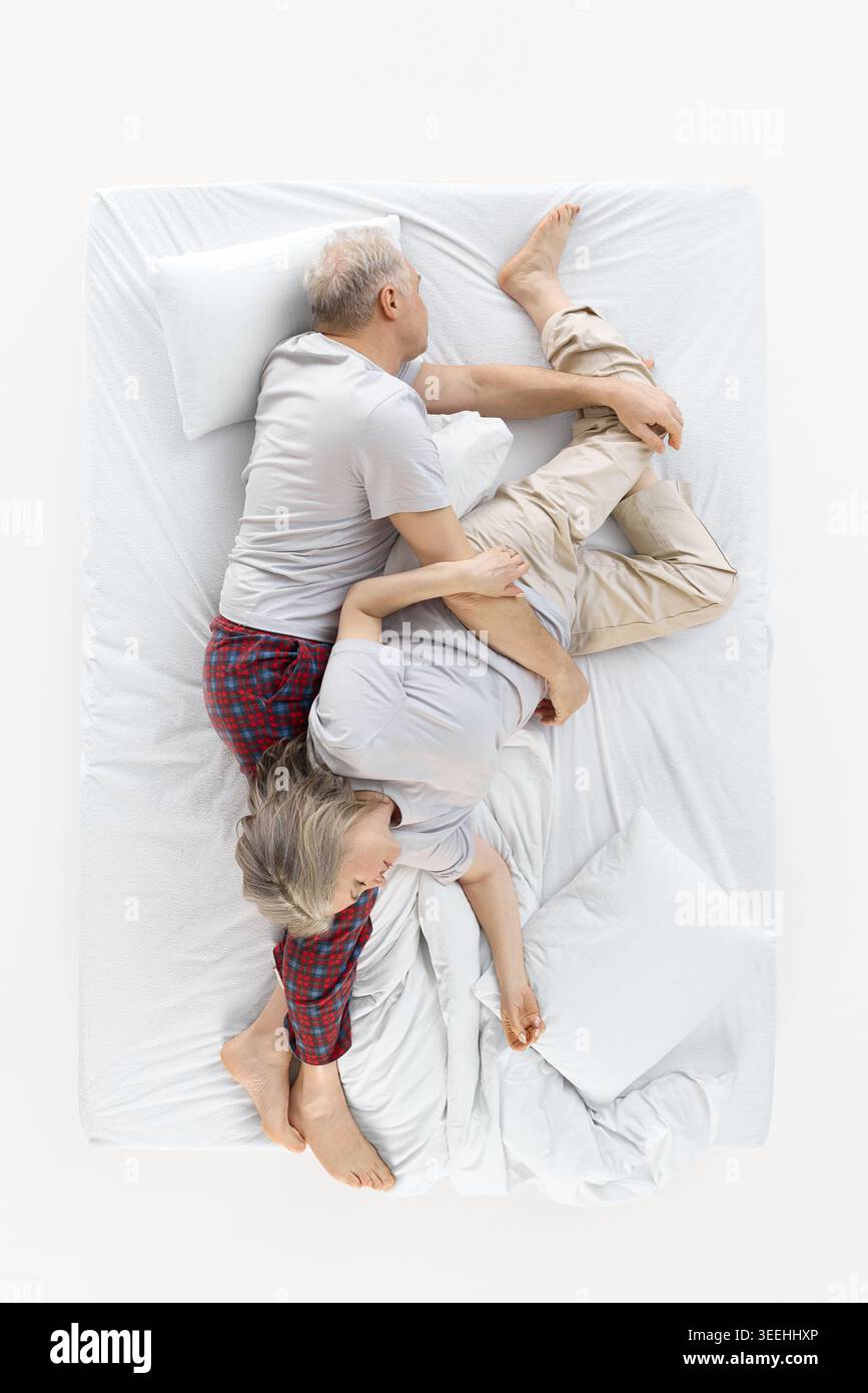 La coppia più anziana dorme in posa aggrovigliata sul letto bianco dall'alto. Foto Stock