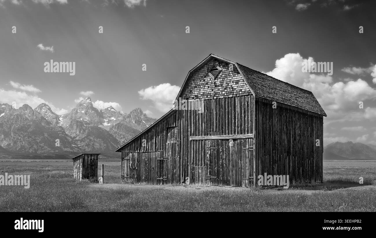 Vecchi fienili in legno abbandonati circondati da praterie e montagne Grand Teton all'orizzonte sotto il cielo blu vicino a Jackson, Wyoming, USA. Foto Stock