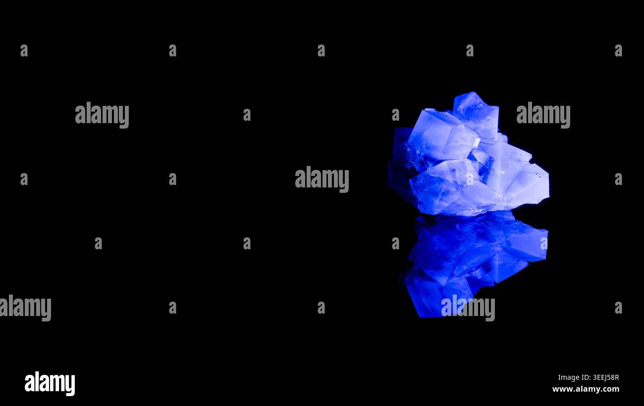 Cristallo di fluorite blu fluorescente sotto la luce UV su sfondo nero con riflesso Foto Stock