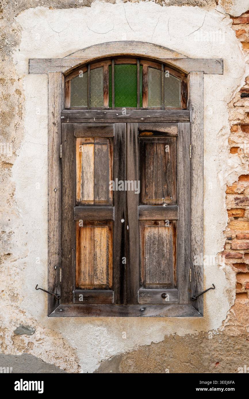 Vista da terra di una cornice rustica di legno arcuato intemprata incastonata in un antico muro di un edificio in gesso, George Town, Penang, Malesia Foto Stock