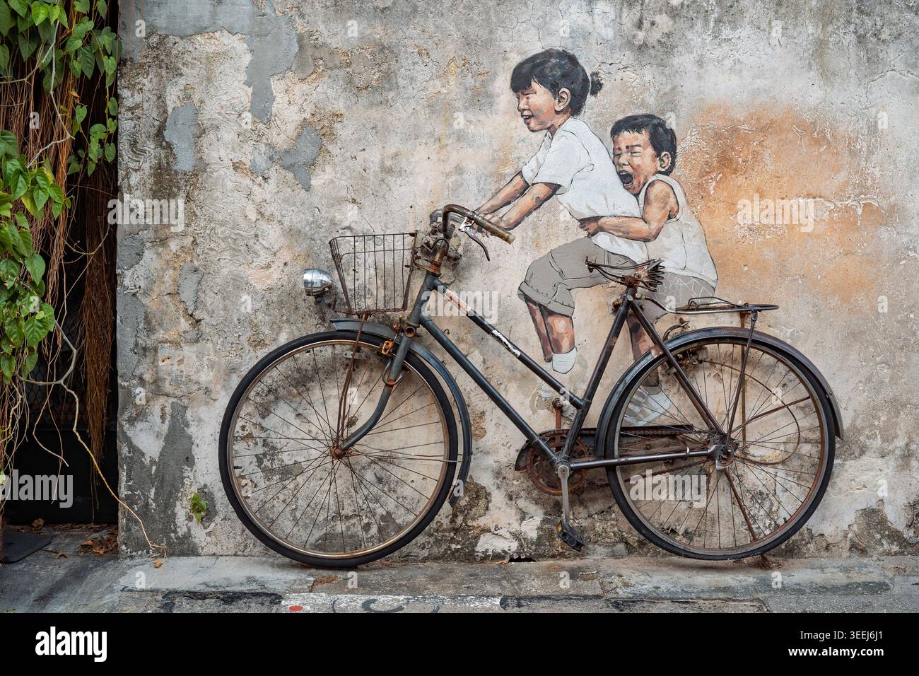 Un noto murale di Street art a George Town, Penang, Malesia, raffigurante due bambini in bicicletta. Le loro espressioni catturano un senso di gioia e. Foto Stock