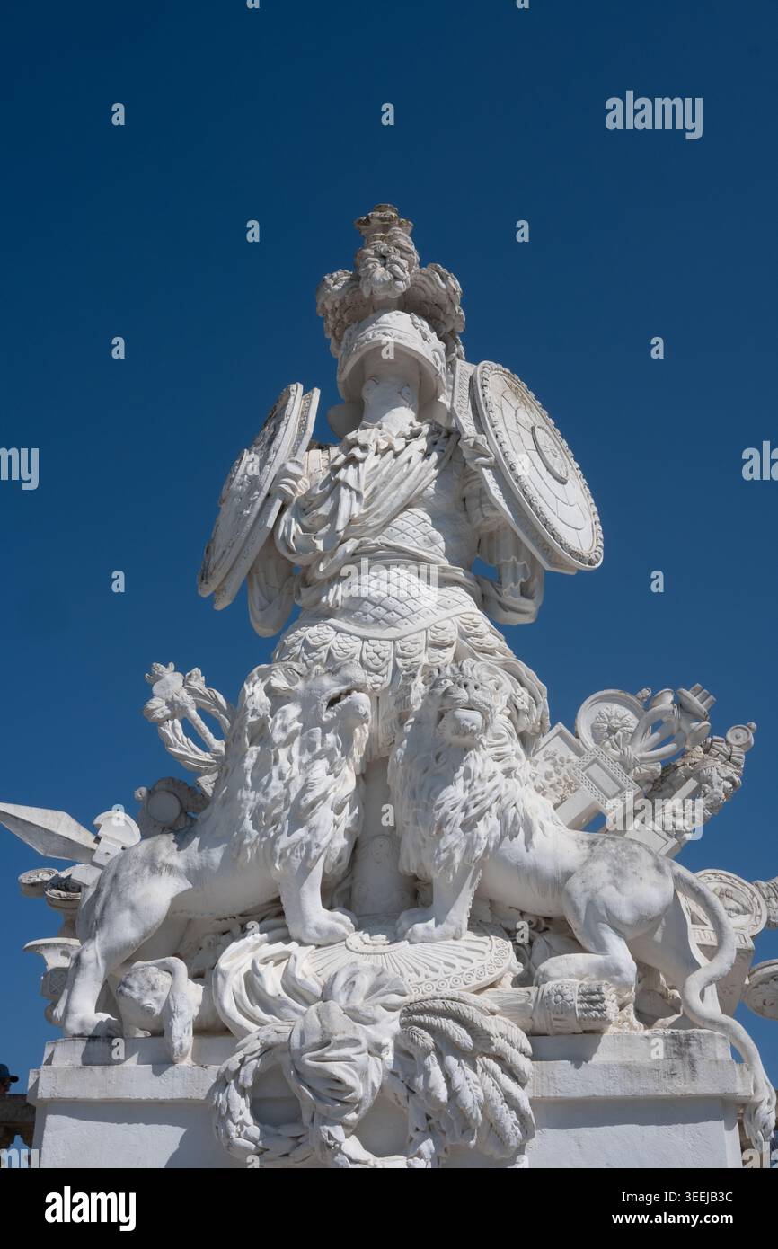 La dettagliata scultura architettonica presenta una figura guerriera con scudi, fiancheggiati da due leoni, adagiati su un cielo azzurro limpido, che mette in risalto la complessità Foto Stock
