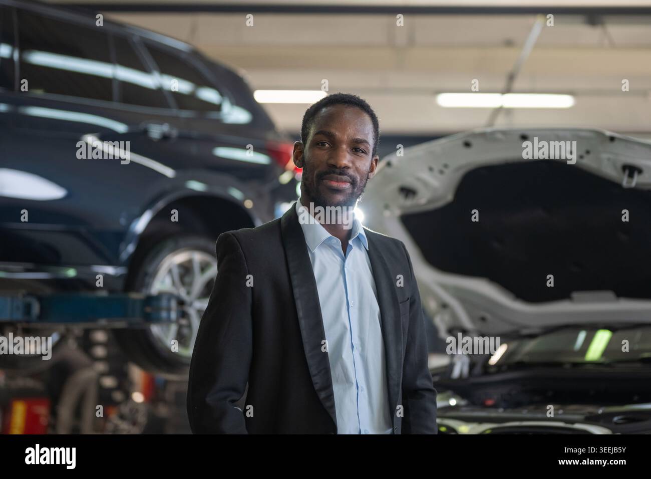 Un uomo d'affari afroamericano ritratto in un'officina di riparazione auto mentre supervisiona le attività di assistenza e ispezione auto. Foto Stock