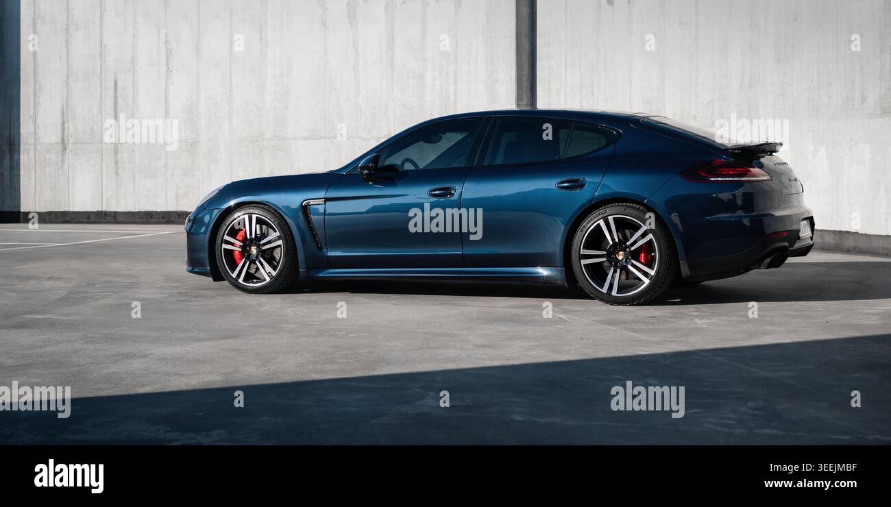 Auto blu scuro nel parcheggio nel pomeriggio di sole. Vista laterale della Porsche Panamera GTS parcheggiata in una città vicino alle mura di cemento di un edificio moderno. Foto Stock
