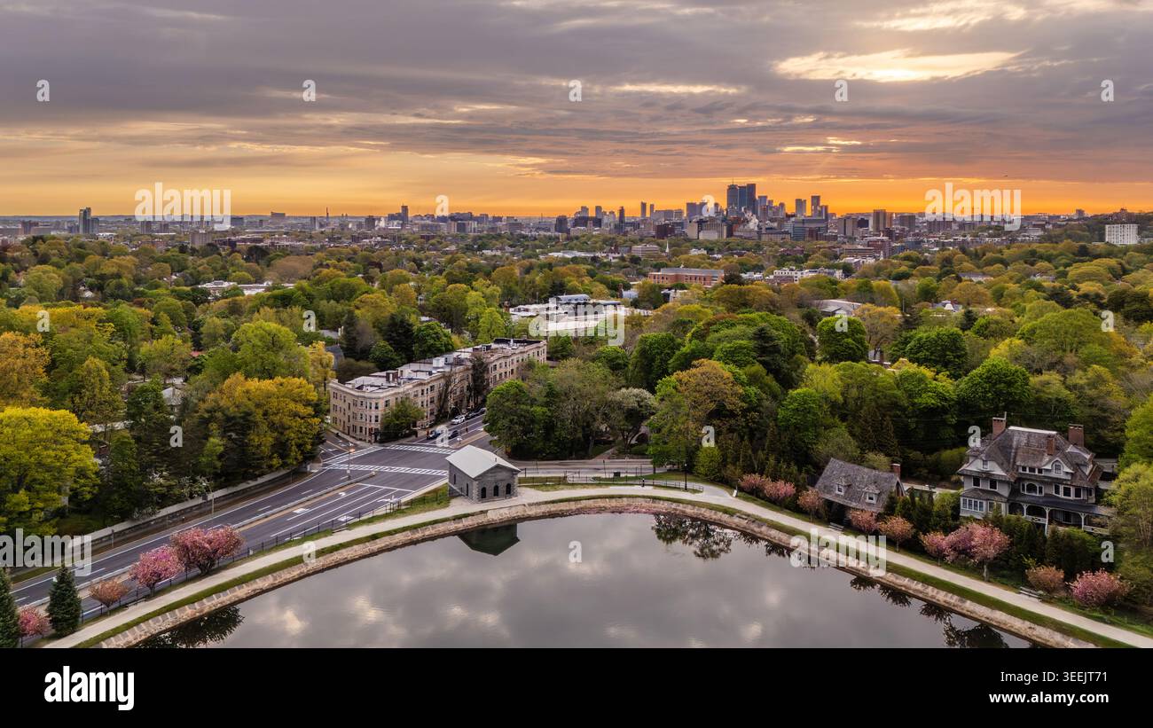 Vista aerea del Brookline Reservoir circondato da lussureggianti ciliegi primaverili e case residenziali con lo skyline di Boston in lontananza all'alba. B Foto Stock