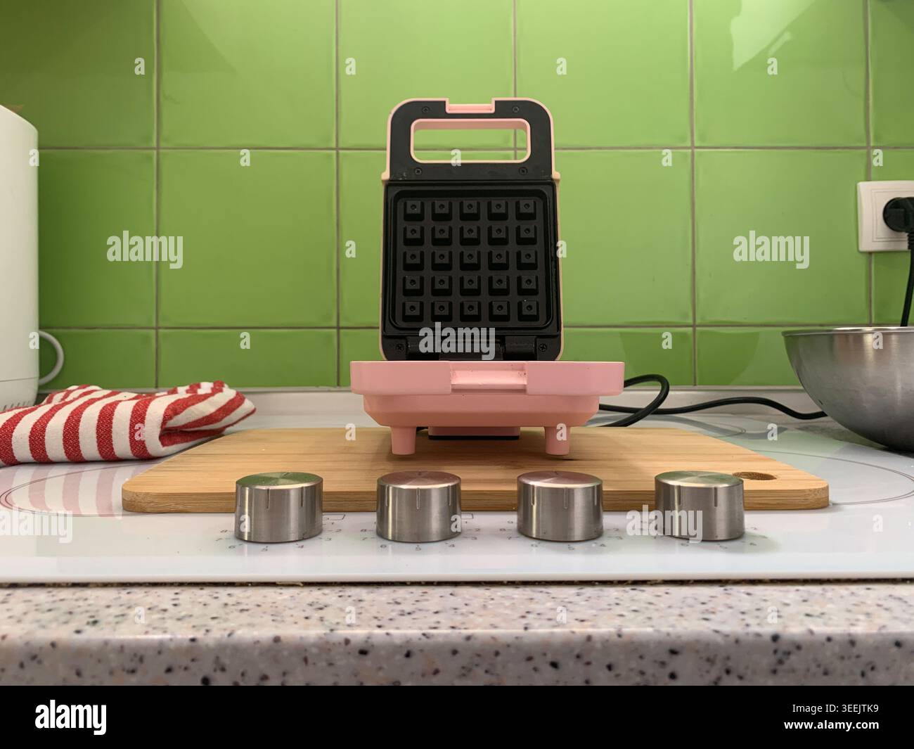 Vista centrata ad angolo basso di una macchina per waffle rosa aperta circondata da quattro piccole tazze metalliche. Foto Stock