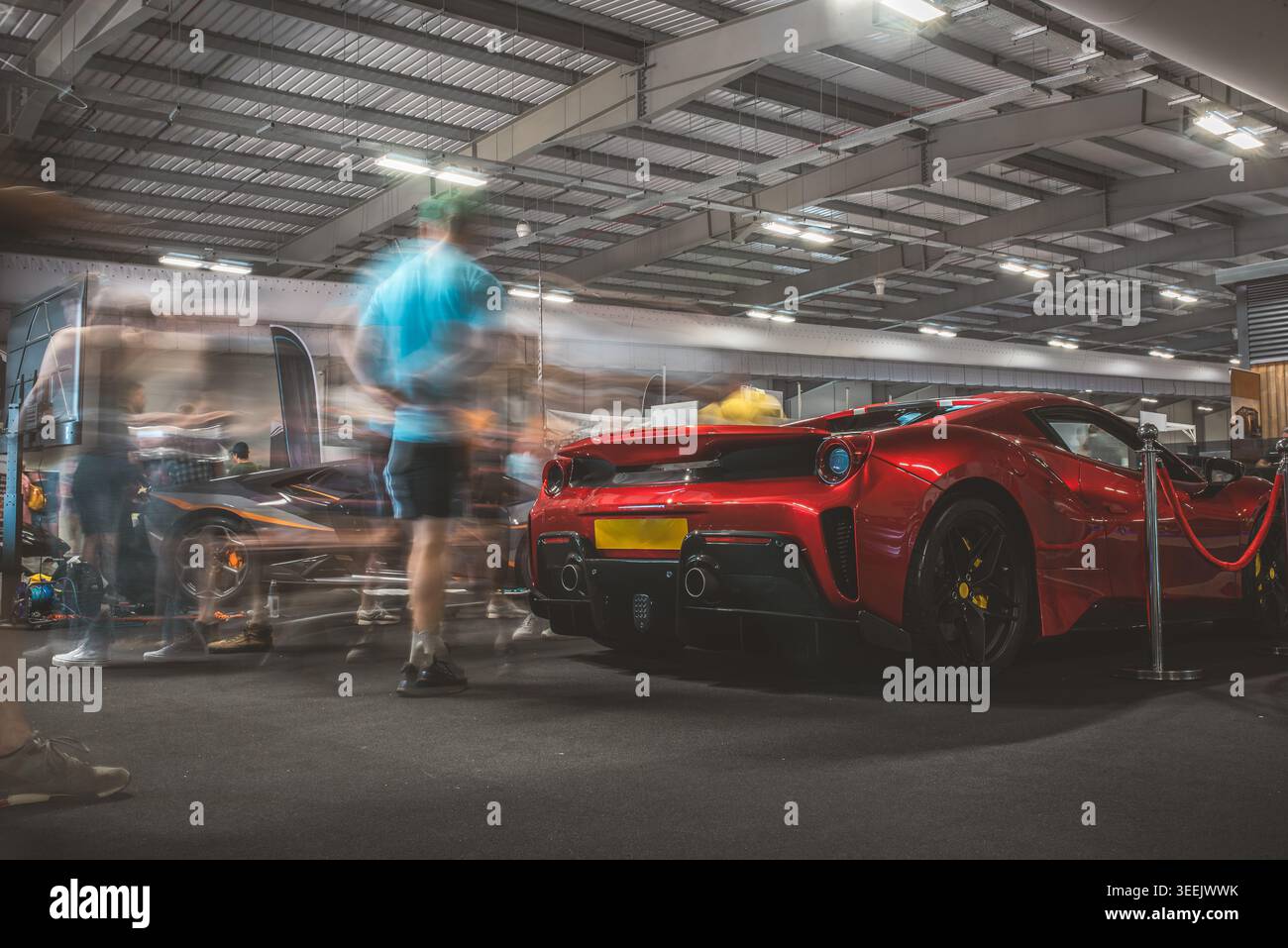 Un'auto sportiva rossa vivace è il punto focale, con la sfocatura del movimento delle persone che crea un senso di movimento Foto Stock