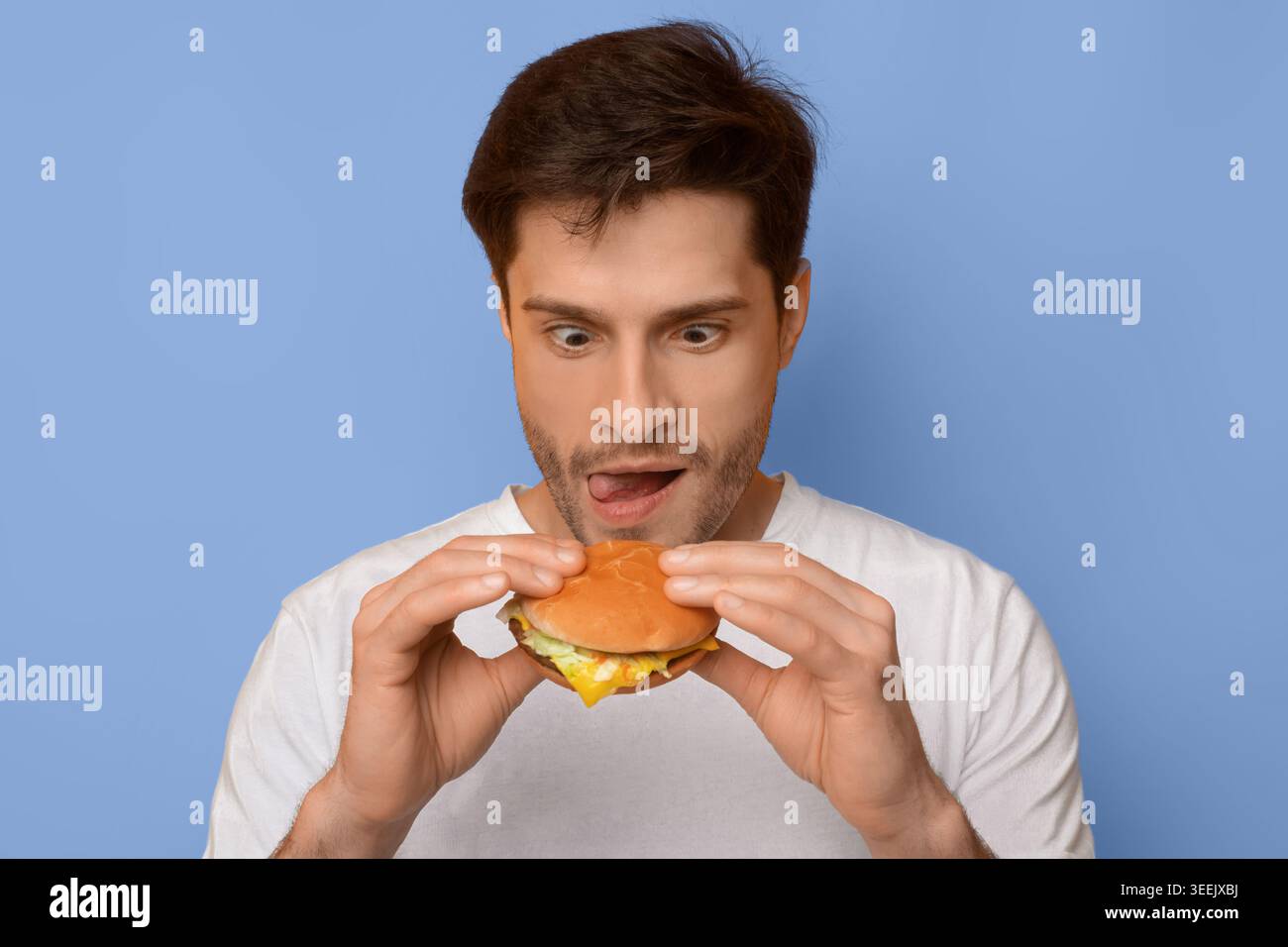 L'uomo si prepara a mangiare un Burger con eccitazione su sfondo blu Foto Stock