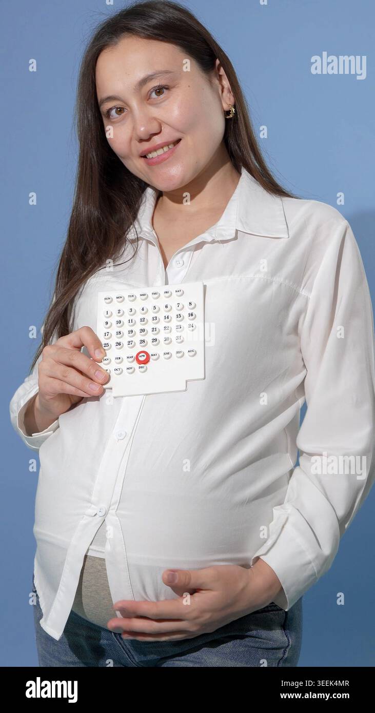 Donna incinta che tiene l'immagine a ultrasuoni contro la parete blu per una professionista Foto Stock