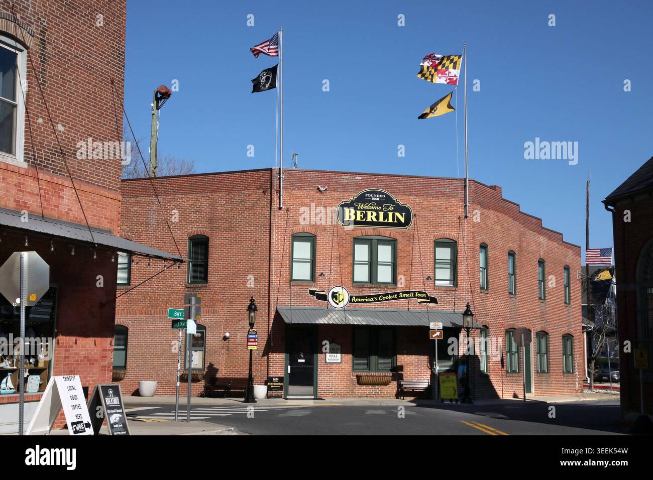 Un basso edificio in mattoni rossi in stile municipale a Berlino, Maryland, con bandiere multiple sopra il tetto, cartello di benvenuto dipinto Foto Stock