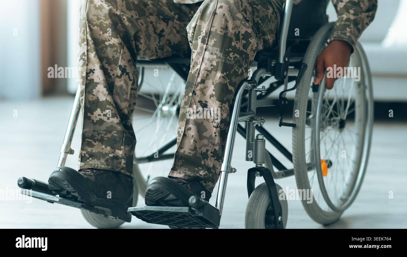 Veterano della sedia a rotelle che indossano pantaloni camouflage che utilizzano la sedia a rotelle al chiuso durante il giorno Foto Stock