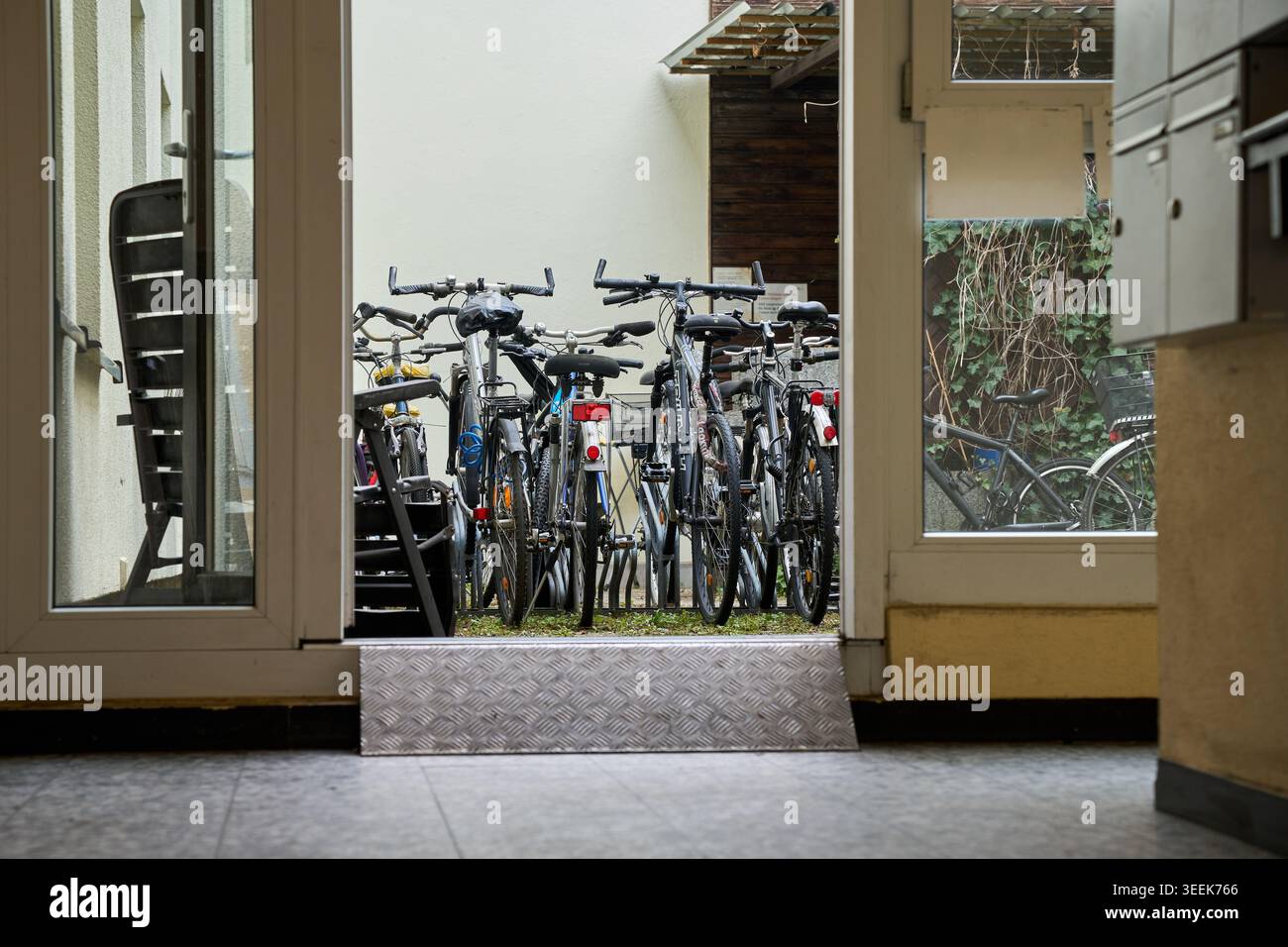 Biciclette parcheggiate in un cortile esterno di un moderno edificio residenziale, con vista da una porta a vetri aperta. Foto Stock