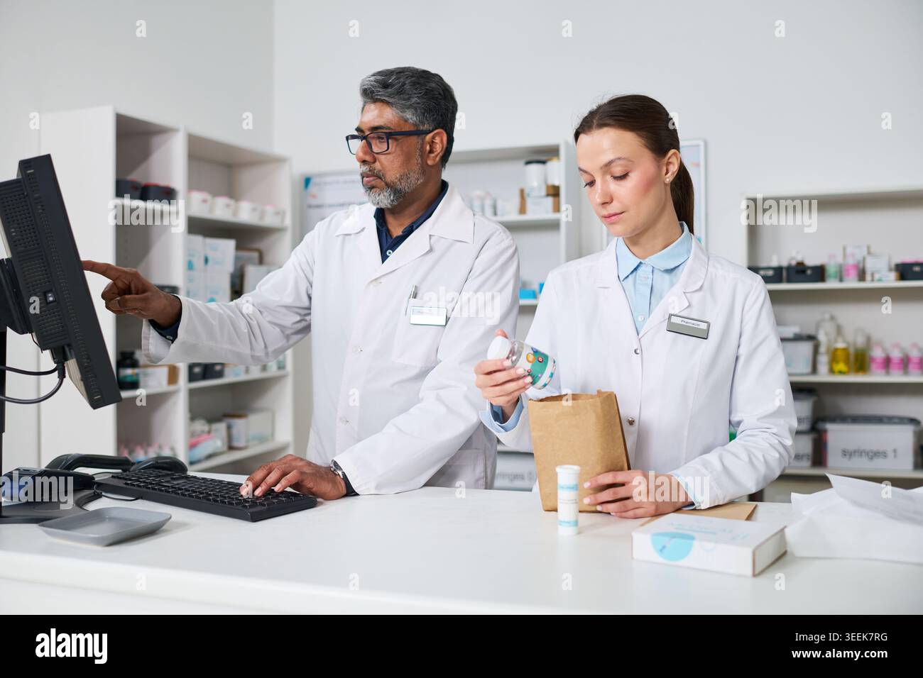 Uomo indiano di mezza età e giovane donna farmacisti che elaborano ordini di prescrizione e controllano l'inventario in farmacia. Per la vendita al dettaglio del settore sanitario, il servizio farmaceutico e il flusso di lavoro del team Foto Stock