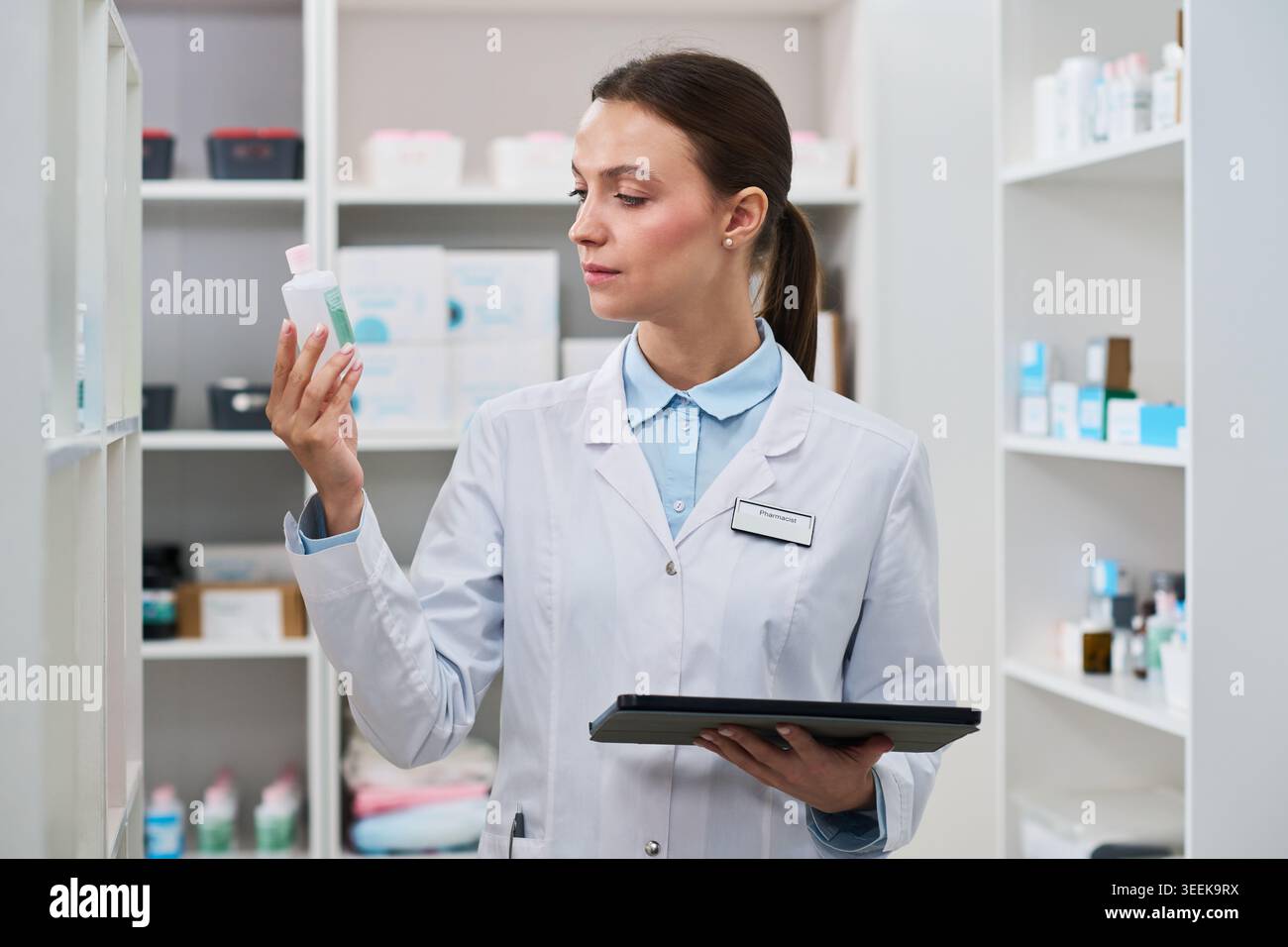 Giovane farmacista che esamina il flacone di medicinali e tiene la compressa in farmacia, gestendo l'inventario e il controllo dei farmaci. Utile per la vendita al dettaglio, il servizio di prescrizione medica, la conformità Foto Stock