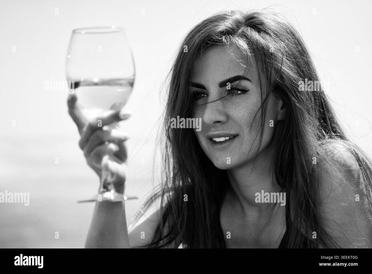 Donna che tiene un bicchiere di vino bianco. Ritratto di una bella signora che si rilassa vicino al mare. Fotografia monocromatica retrò con grana della pellicola. Stile di vita vintage, drin Foto Stock