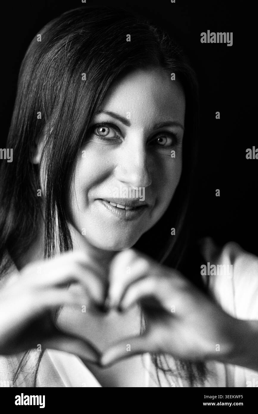 Donna che fa gesti cardiaci con la mano. Ritratto di una donna sorridente che esprime amore e cura. Concetto romantico. Fotografia monocromatica con grana analogica e Foto Stock