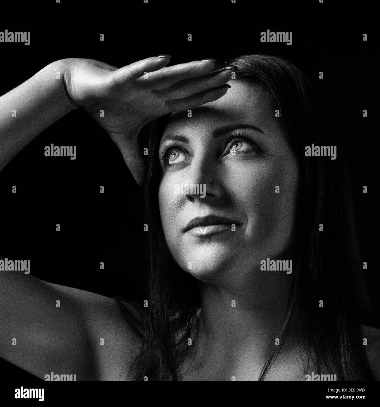 Donna che guarda in lontananza con la mano sulla fronte. Ritratto della signora che protegge gli occhi dalla luce intensa. Fotografia in bianco e nero in stile retrò wi-fi Foto Stock