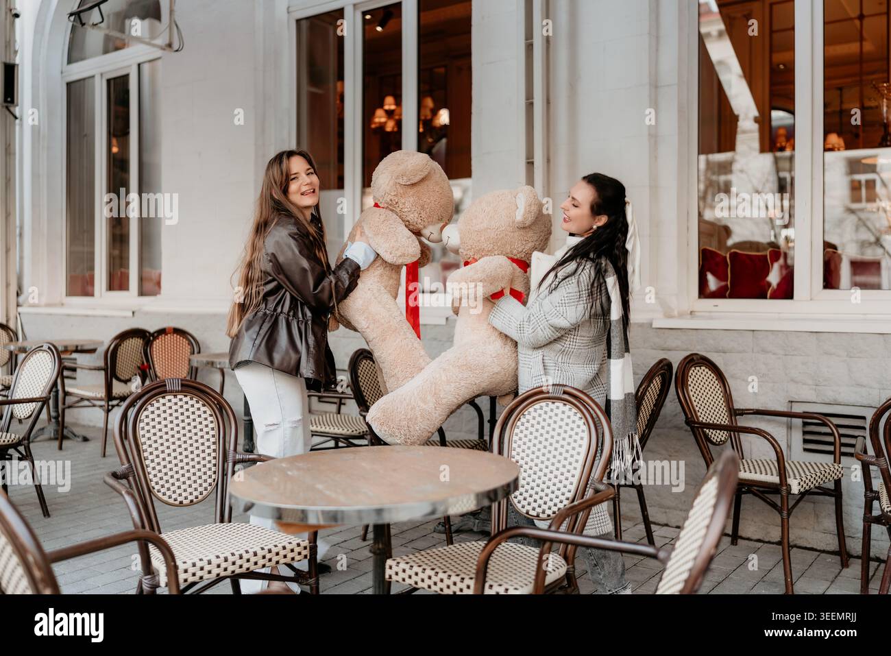 Friends Teddy Bear Cafe patio con due giovani donne sorridenti che tengono in mano giocattoli di peluche giganti durante una gioiosa gita invernale Foto Stock