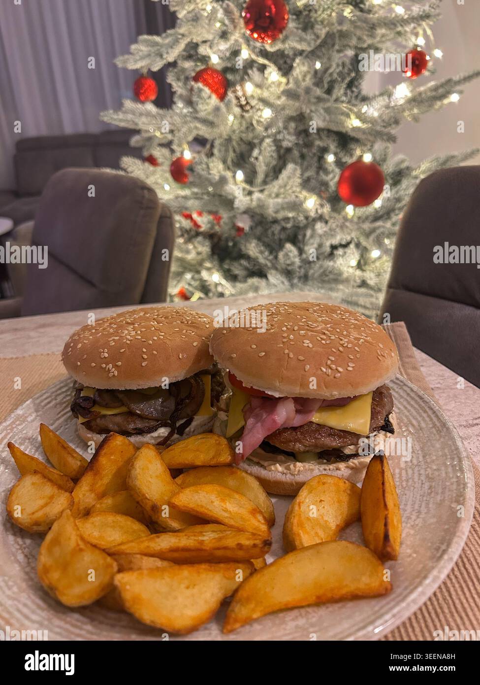 Hamburger fatti in casa con patate a cubetti serviti su un tavolo con un albero di Natale luminoso sullo sfondo. - Immagine stock catturata con smartphone