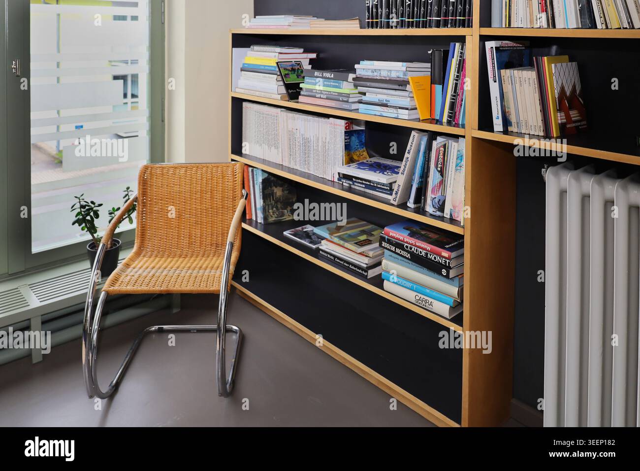 Design Bauhaus alla Haus Rabe di Zwenkau: Libreria piena di libri d'arte accanto a una sedia a sbalzo in vimini e tubolare in acciaio cromato Foto Stock