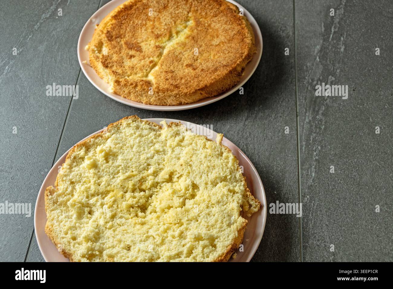 Torta di spugne fatta in casa appena sfornata tagliata a strati e preparata per assemblare una torta alla fragola in un vero ambiente di cucina casalingo. Foto Stock