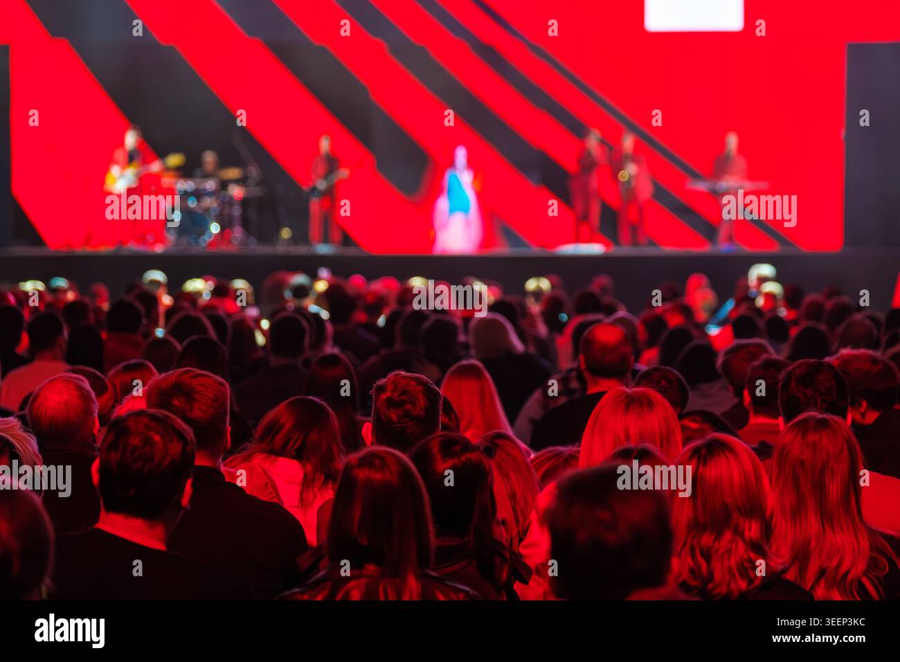 Una grande folla guarda i concerti dal vivo, la band si esibisce sul palco sotto una spettacolare luce rossa e immagini. Foto Stock