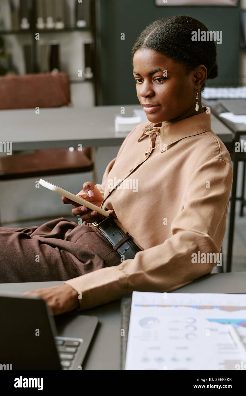 Donna adulta di colore che utilizza lo smartphone per le comunicazioni aziendali Foto Stock