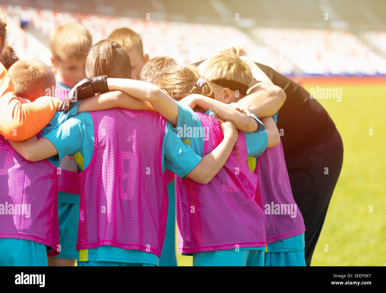 Squadra giovanile di calcio nei giubbotti di allenamento rosa e allenatore in Huddle prima della partita - Junior Football Players lavoro di squadra e motivazione in Professional Stadium Foto Stock
