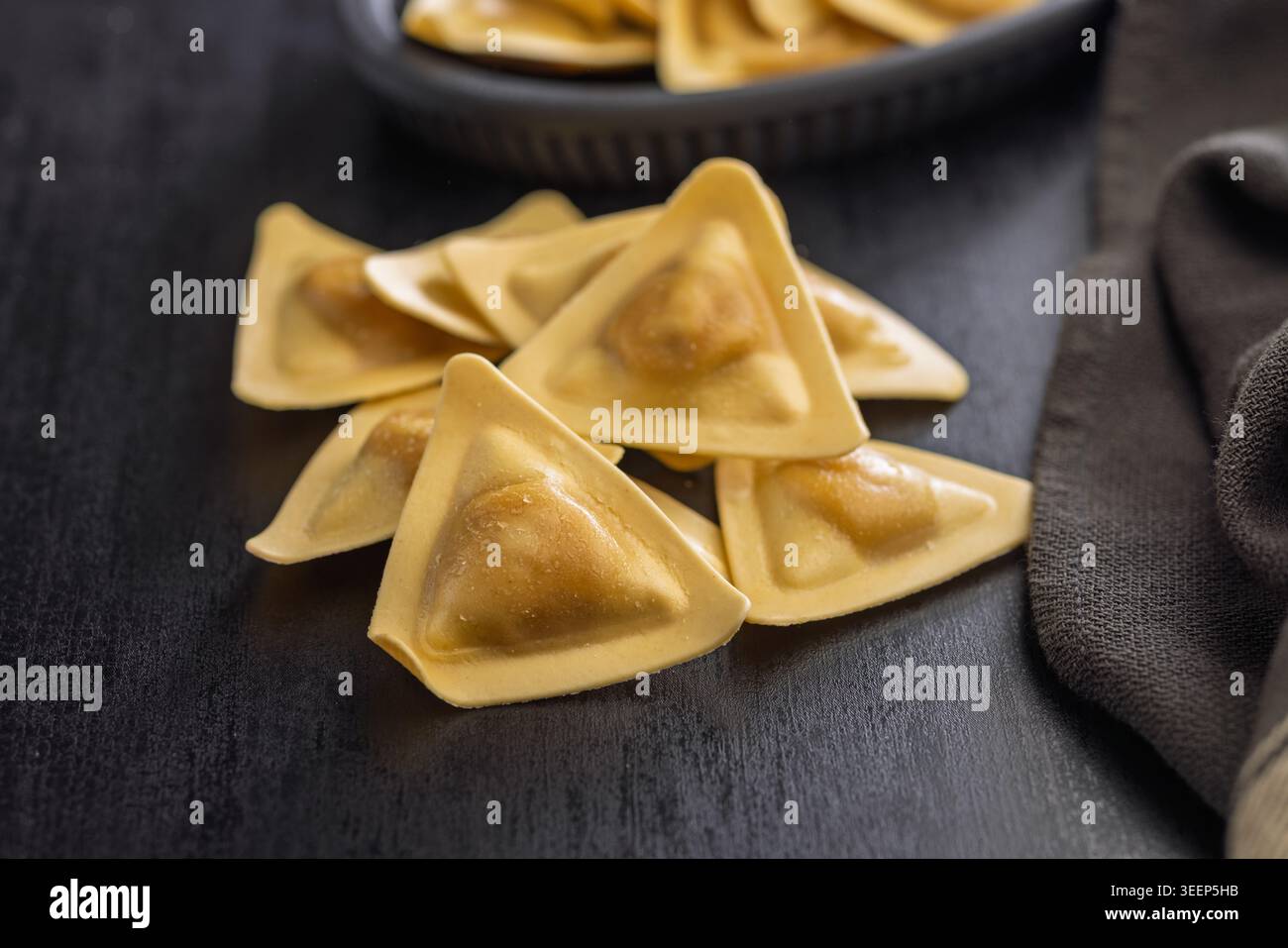 Primo piano di ravioli triangolari su una superficie di legno scuro, evidenziando la pasta ripiena cruda con impasto dorato. Ideale per la cucina italiana, ricetta visua Foto Stock