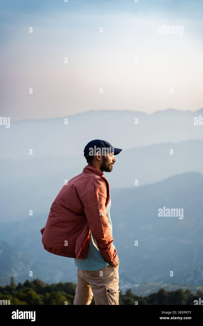 Un uomo barbuto che indossa un berretto e una giacca si affaccia sulle nebbiose catene montuose di Raghupur Fort, Sojha, Manali, Himachal Pradesh, India. Foto Stock