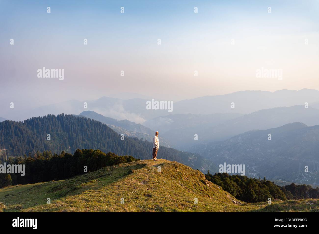 Persona in piedi su una montagna erbosa che si affaccia sulle valli nebbiose di Raghupur Fort, Sojha, Manali, Himachal Pradesh, India. Foto Stock