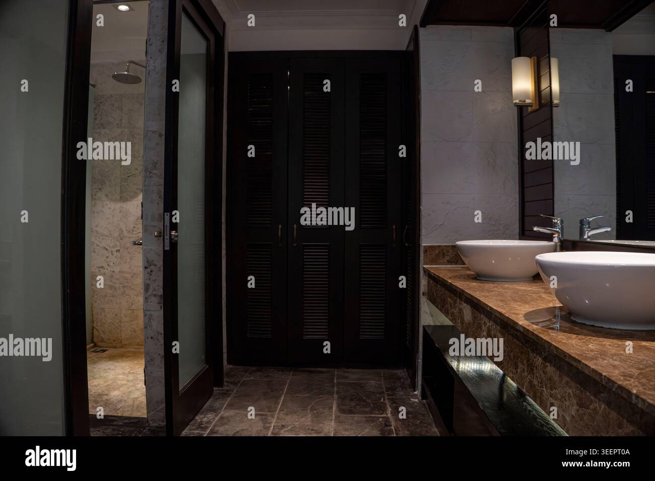 Bagno di lusso in Vietnam con lavandino doppio su ripiano in marmo, porte dell'armadio con persiane scure, cabina doccia in vetro e pareti piastrellate in marmo Foto Stock
