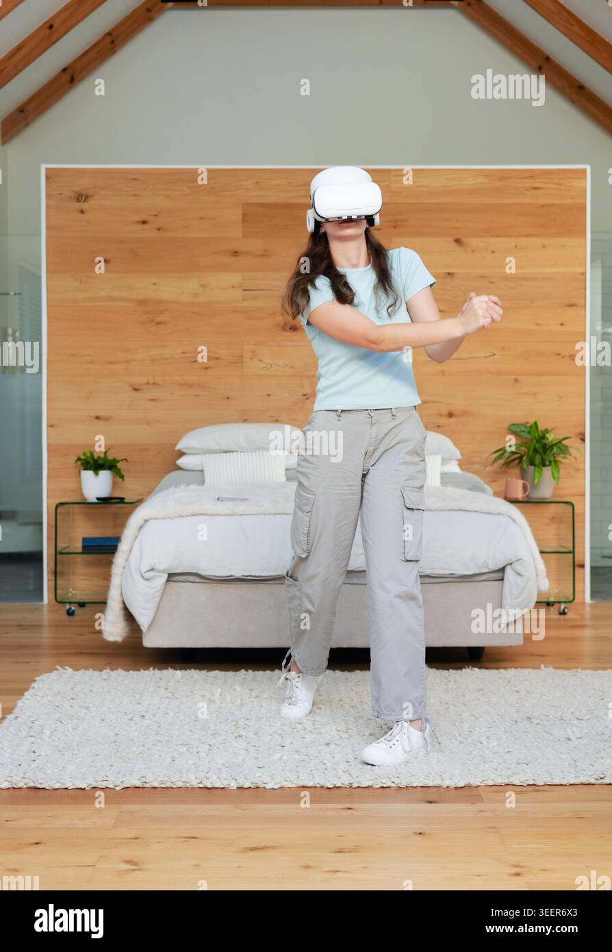 Donna in piedi centrata in camera da letto con visore VR bianco e che interagisce con oggetti virtuali Foto Stock