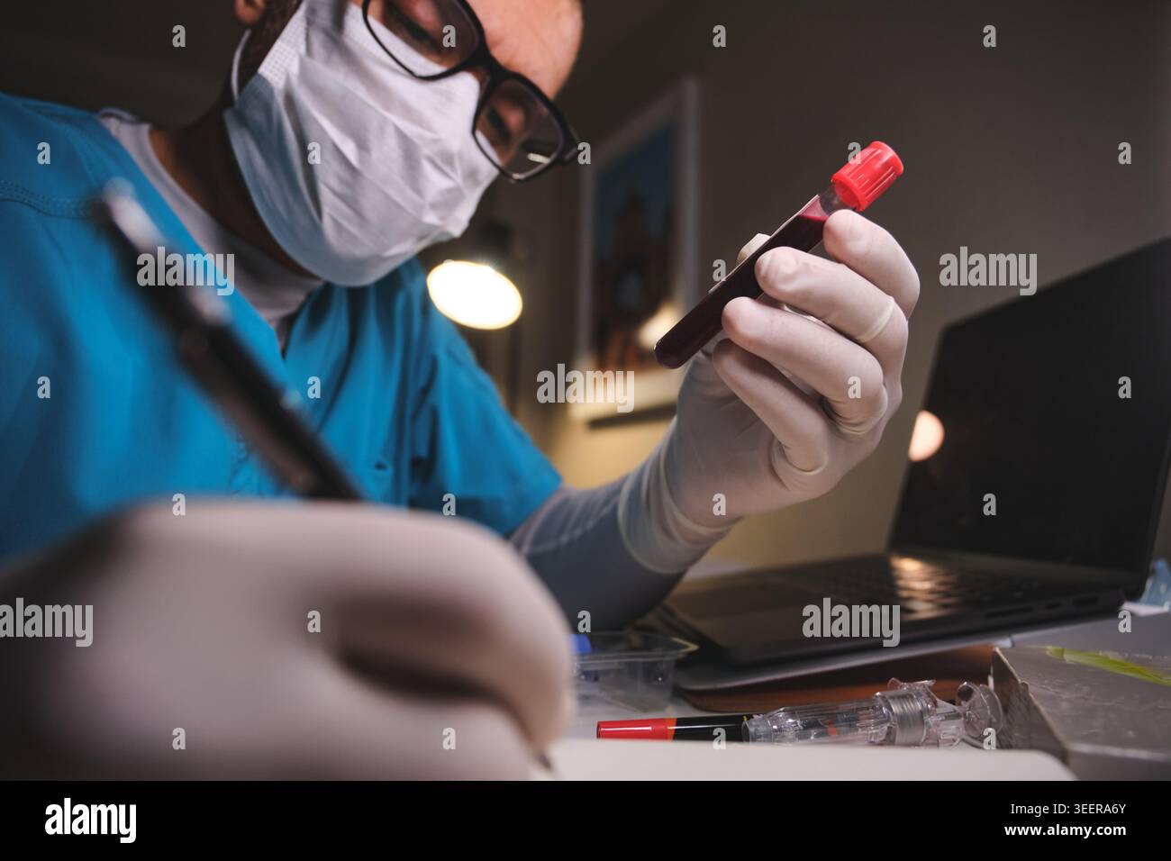 Operatore sanitario che indossa maschera protettiva e guanti che esaminano una fiala di sangue e scrivono note Foto Stock