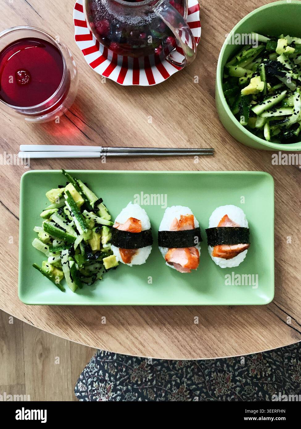 Il cibo è disposto su un piatto verde con insalata a base di nori, cetrioli e avocado, accanto al sushi nagiri ricoperto di pesce rosso, adatto per la colazione Foto Stock