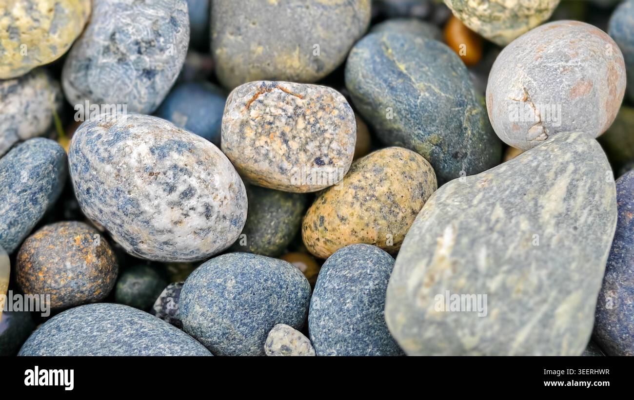 Primo piano su un mucchio di rocce marine lisce assortite. Texture diverse e delicati colori blu, grigio e abbronzatura sotto un'illuminazione soffusa. Adatto per gli ambienti o per il natu Foto Stock