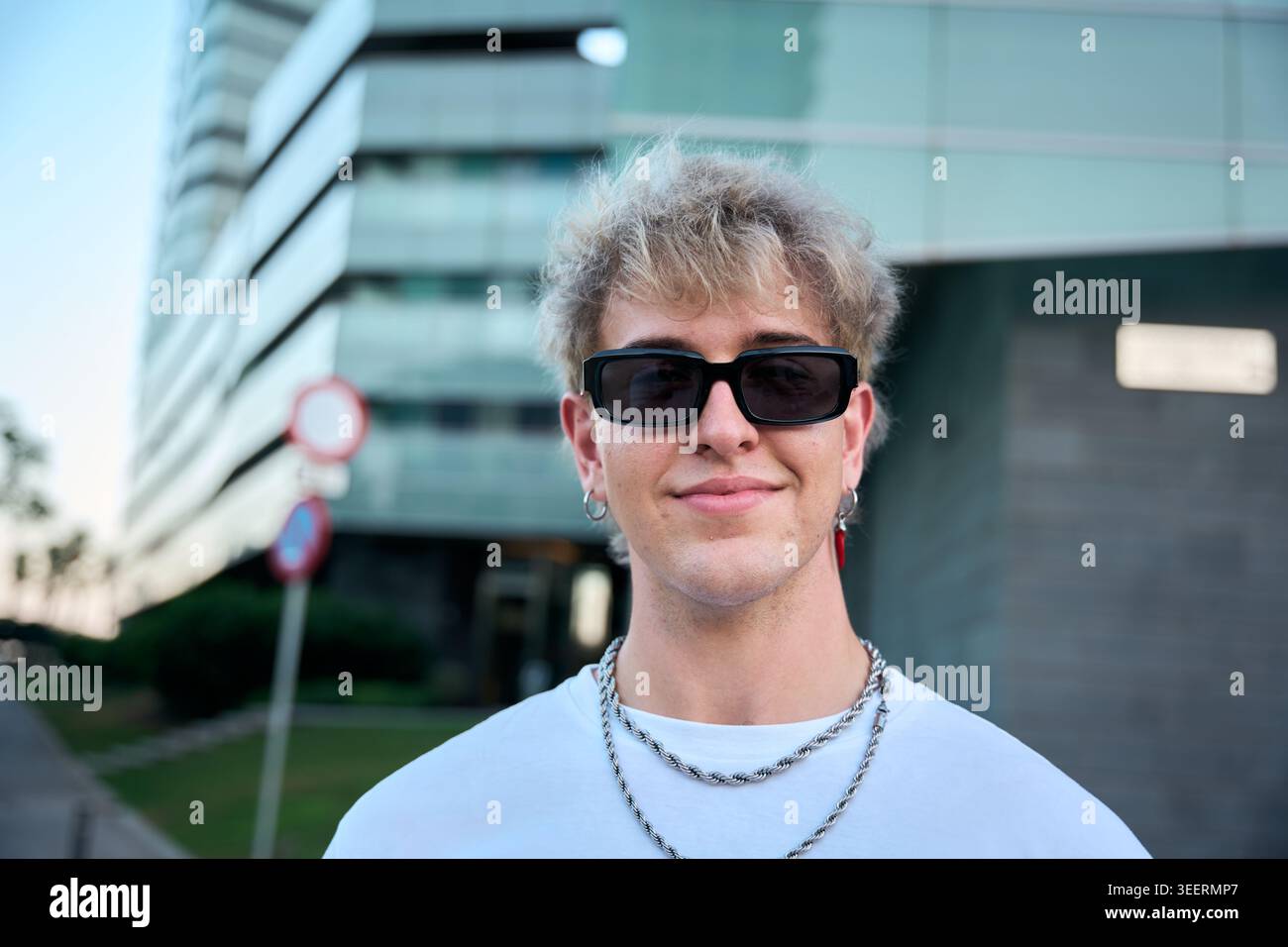 Bionda gen z influencer sorridente indossando occhiali da sole e catene d'argento Foto Stock